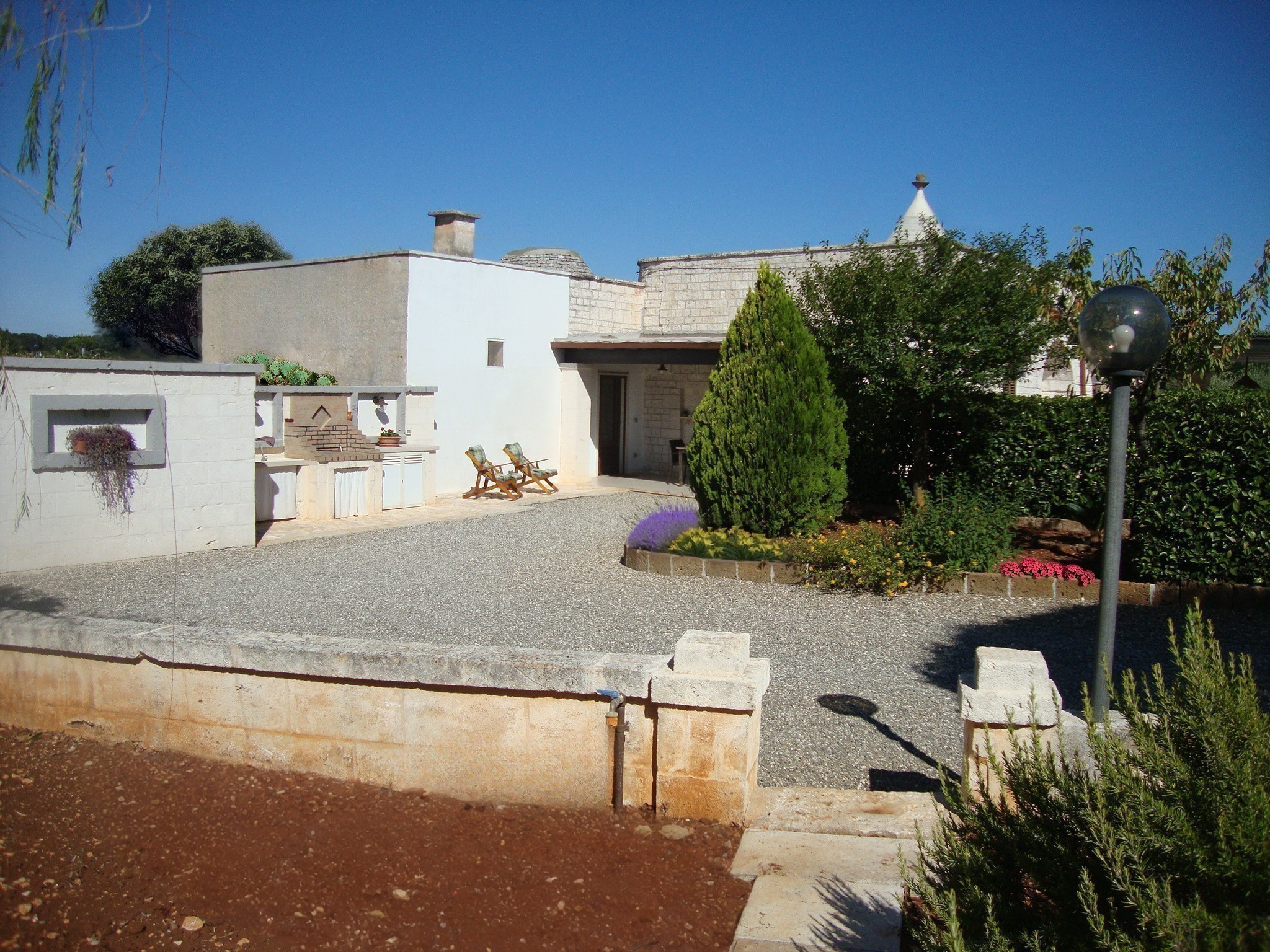 Ingresso e giardino del Trullo Il Nido con cucina esterna attrezzata e cono del trullo sullo sfondo