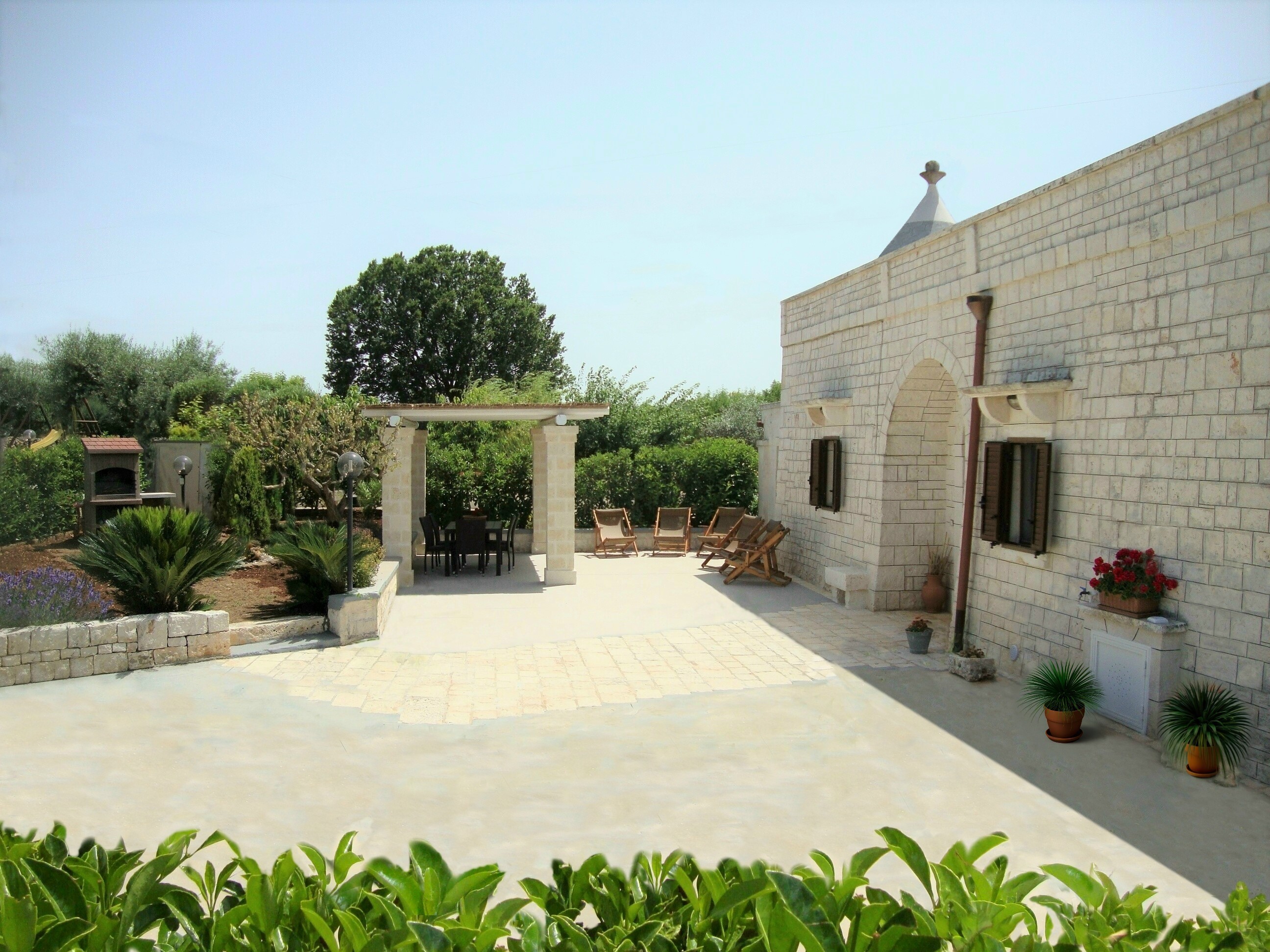 Piazzale esterno del Trullo Incanto con pergola, tavolo da pranzo e braciere